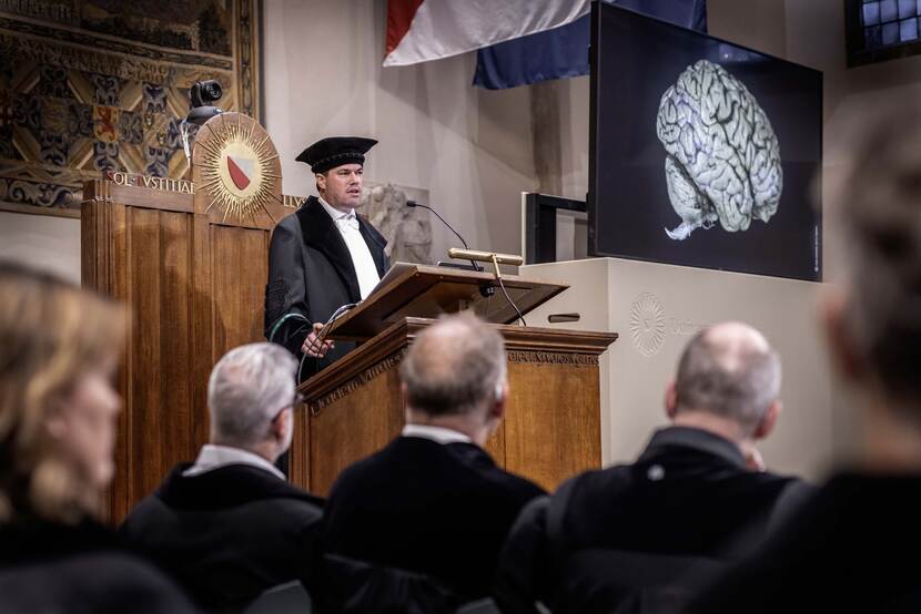 Professor Elbert Geuze tijdens zijn oratie met op het beeldscherm naast hem een afbeelding van een brein